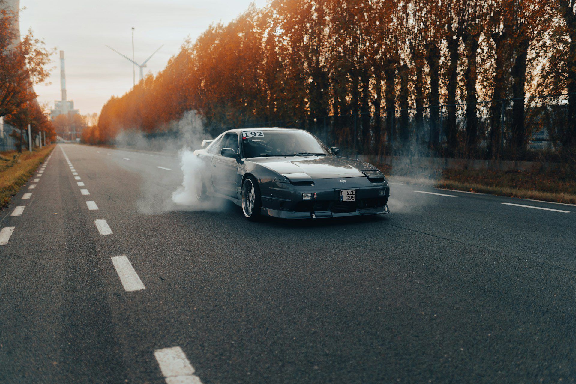 Black sports car drifting on a quiet road, surrounded by autumn trees and smoke.