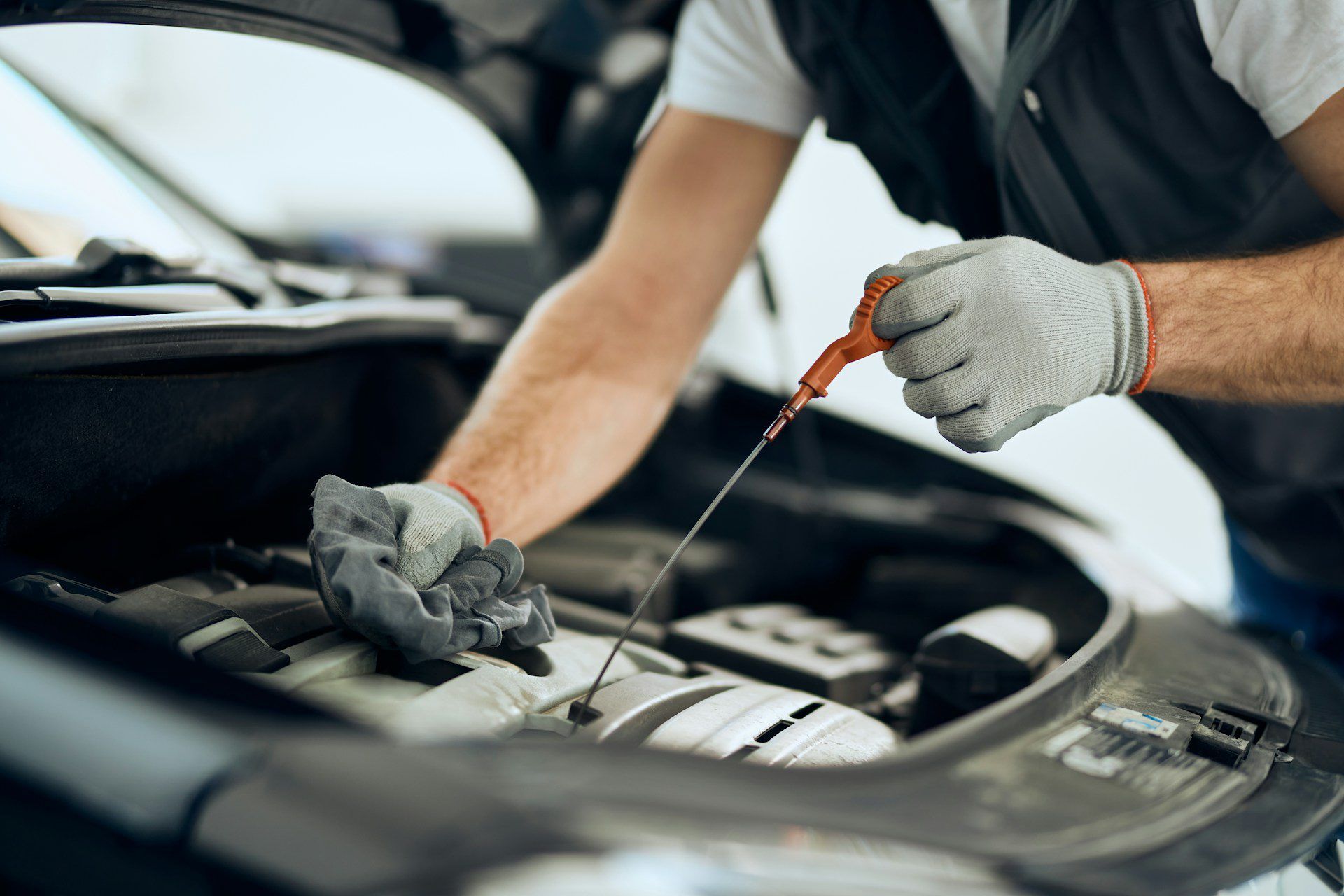 Mechanic checks engine oil level with a dipstick under the hood of a car.