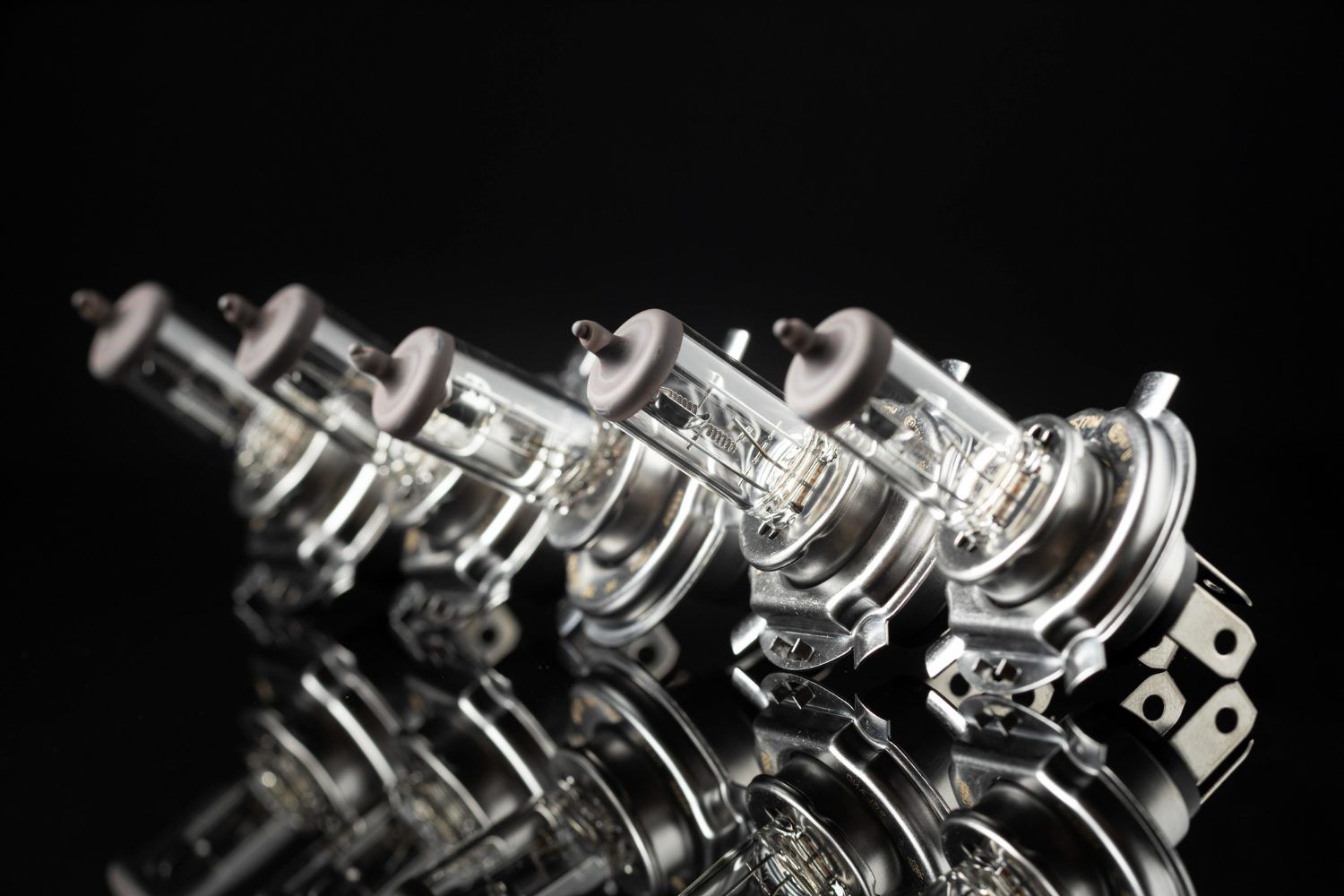 Five automotive headlight bulbs arranged in a row, reflecting on a dark surface.