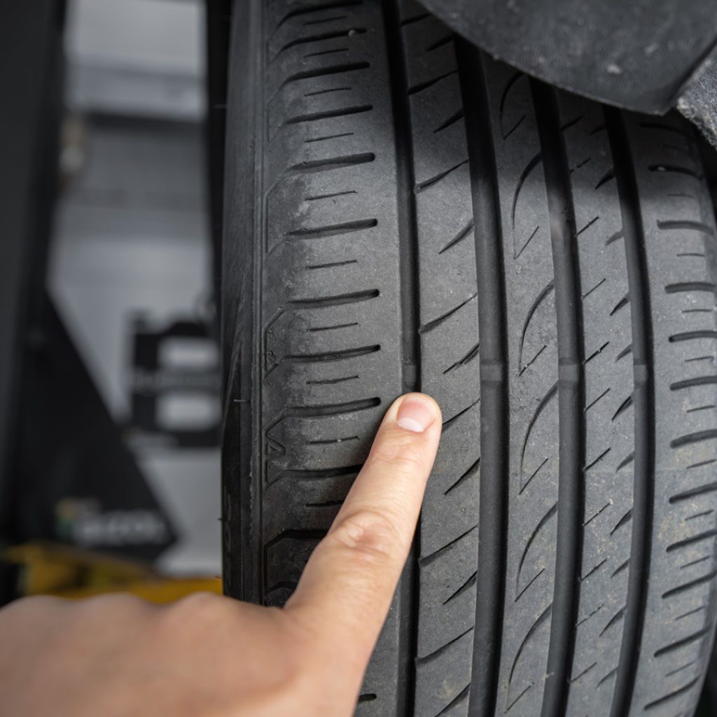 A person pointing to uneven tread on a tire, which is what happens when you ignore alignment issues. 