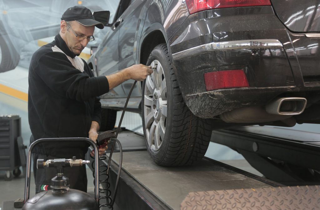 An auto mechnic in Albuquerque checks the air pressure of a car's tire as part of routine maintenance. 