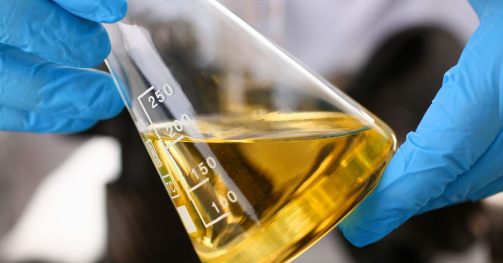 A person in a lab holds a beaker full of synthetic motor oil used during Albuquerque oil changes instead of conventional oil. 