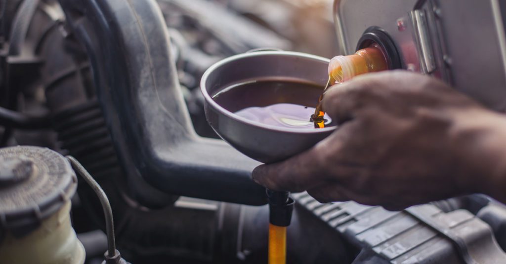 A man pours fresh motor oil into his engine after changing the oil himself. 