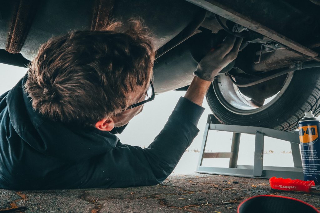 A man lays under a car to drain the oil pan before doing an oil change with either conventional or synthetic oil. 