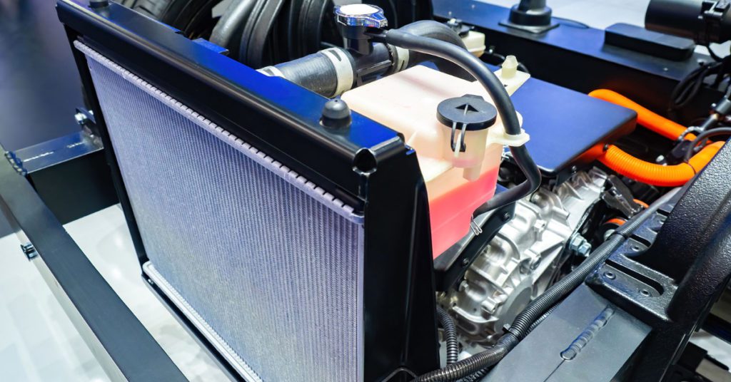 A brand new radiator sits next to a vehicle that's waiting to receive it. 