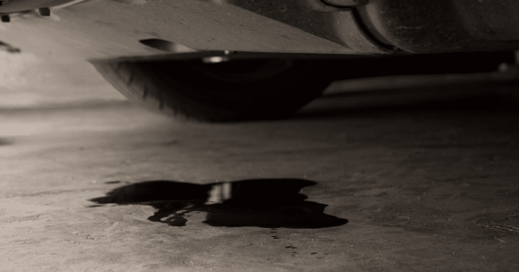 A puddle of engine oil lays on a cement floor underneath a car, indicating it's time to call for engine repair in Albuquerque. 